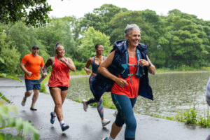 Runners taking part in a community fun run in the rain. They are smiling as they run and follow each other on a path.
