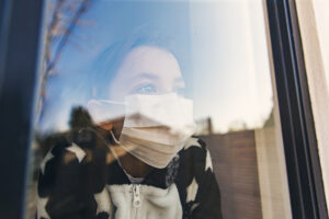 Woman in face mask looking out of a window