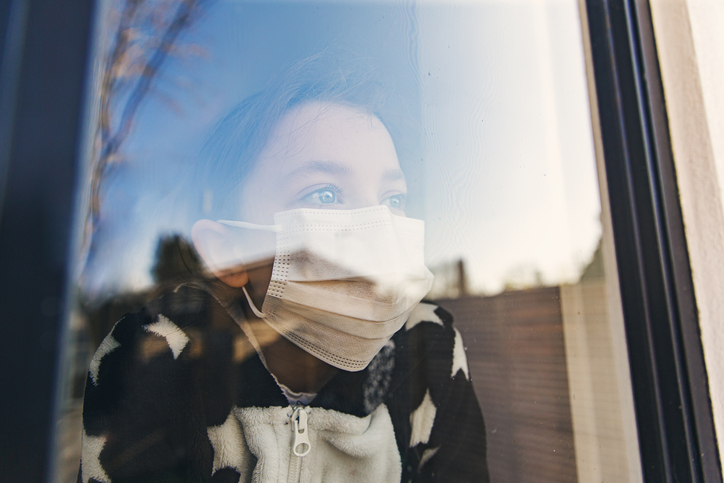 Woman in face mask looking out of a window