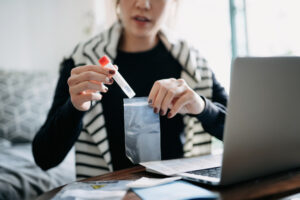 Cropped shot of young Asian woman consulting to her family doctor online in a virtual appointment holding a medical test tube conducting Covid-19 diagnostic test at home