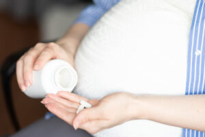 pregnant woman sits in a chair at home holding a jar of pills in her hands