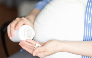 pregnant woman sits in a chair at home holding a jar of pills in her hands