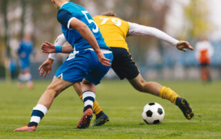 Football Players Compete in Tournament Match in a Duel Football Game on Summer Sunny Day Adul Soccer Players in Blue and Yellow Jersey Uniforms Running Classic Soccer Ball on Grass Pitch