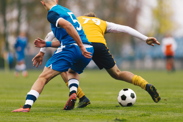 Football Players Compete in Tournament Match in a Duel Football Game on Summer Sunny Day Adul Soccer Players in Blue and Yellow Jersey Uniforms Running Classic Soccer Ball on Grass Pitch