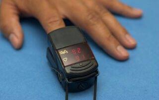 brown skinned hand with pulse oximeter on index finger