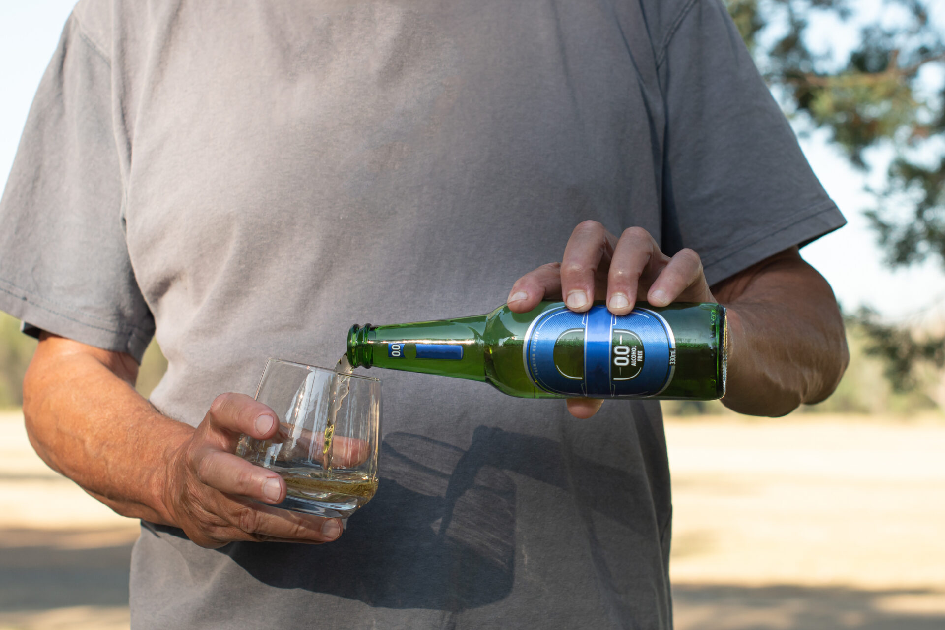Man pouring a bottle of blue label 00 alcohol free beer into a glass on a hot sunny day