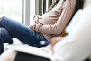 Pregnant young woman waits with unrecognizable female social worker