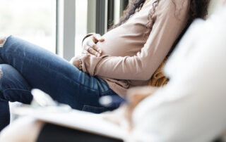 Pregnant young woman waits with unrecognizable female social worker