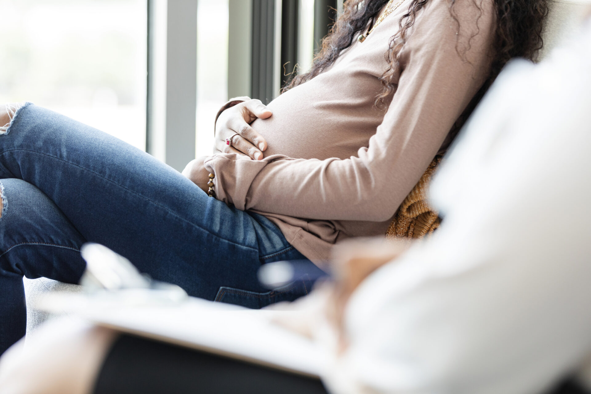 Pregnant young woman waits with unrecognizable female social worker
