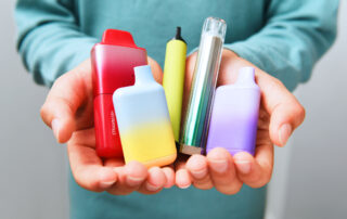 Close up of hands holding a variety of disposable vapes
