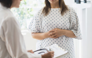 Close up image of a doctor taking notes and a female patient in a hospital gown
