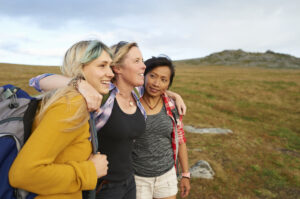 A group oF female hiking friends huddle together on a rocky moorland in the countryside.