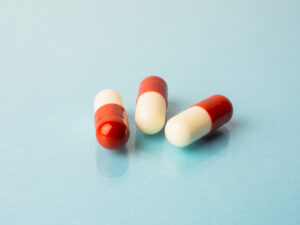 Three red and white capsule pills laying on a flat blue surface