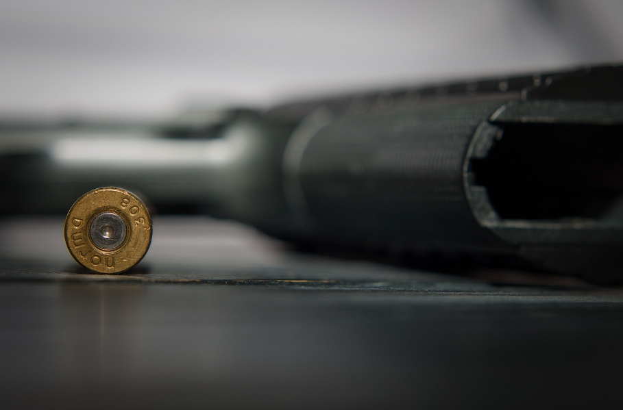 A pistol lying on a table with a bullet beside it
